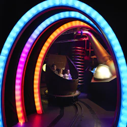 Människor i en temapark åker fordon genom en tunnel med färgglada LED-BÅGAR i en mörk miljö med sci-fi-tema.