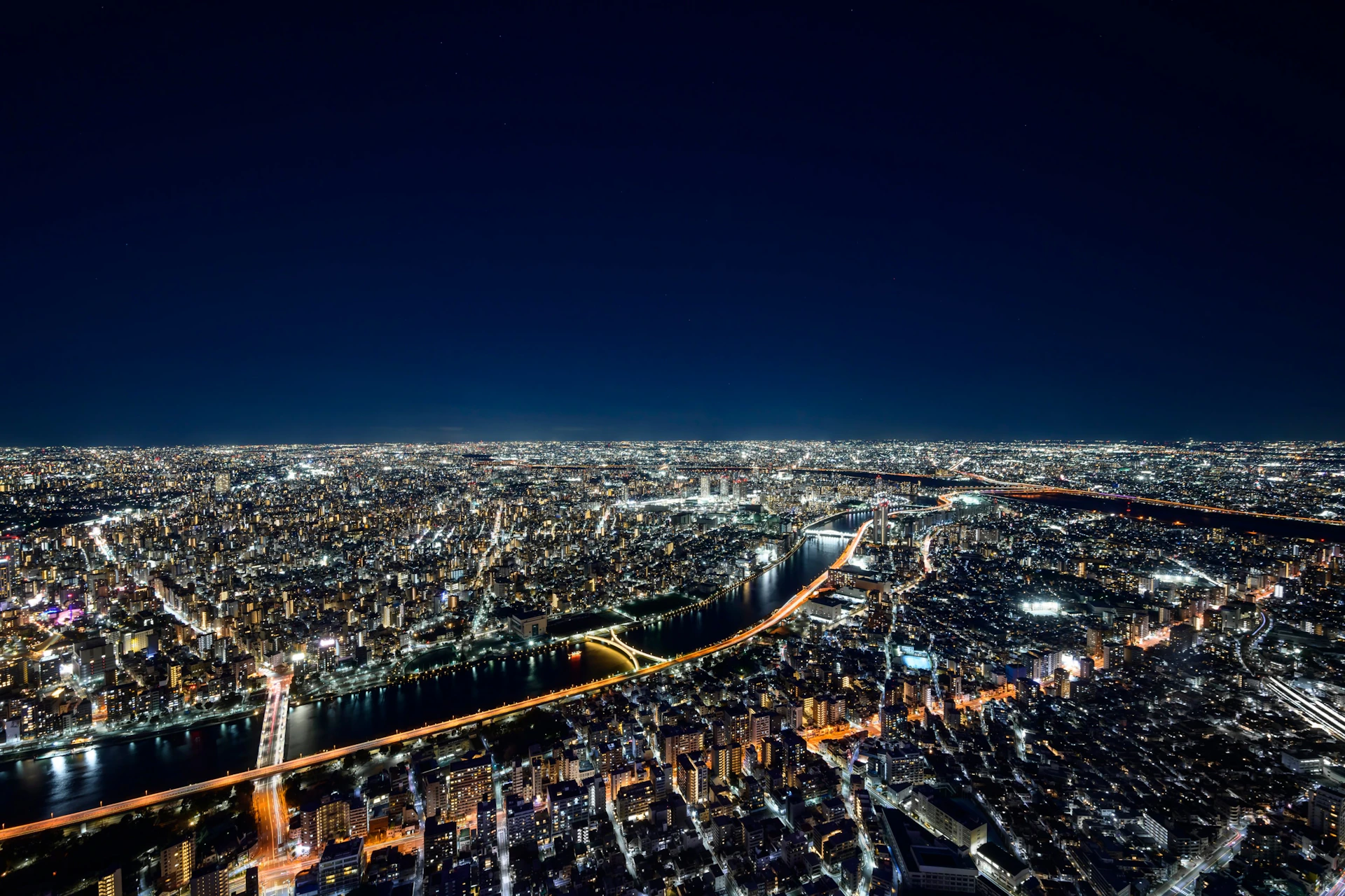 Aerial view of a city at night with illuminated streets, buildings, and a lit bridge crossing a river.
