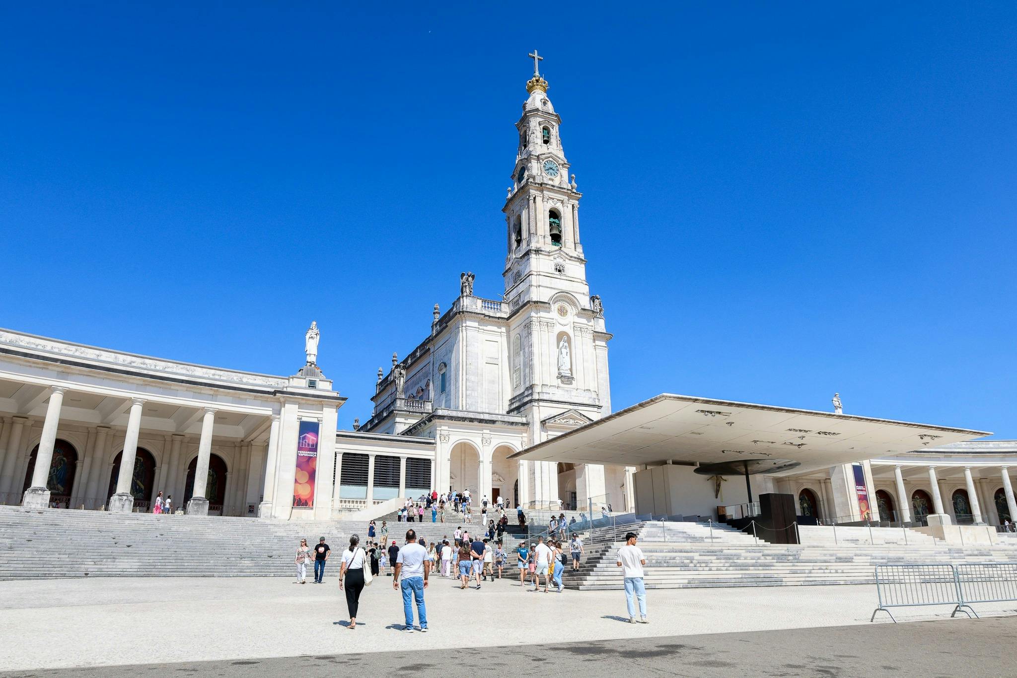 観光客は、澄んだ青い空の下、高い鐘楼のある大きな華やかな教会の近くを歩いています。 入場口までの段差。