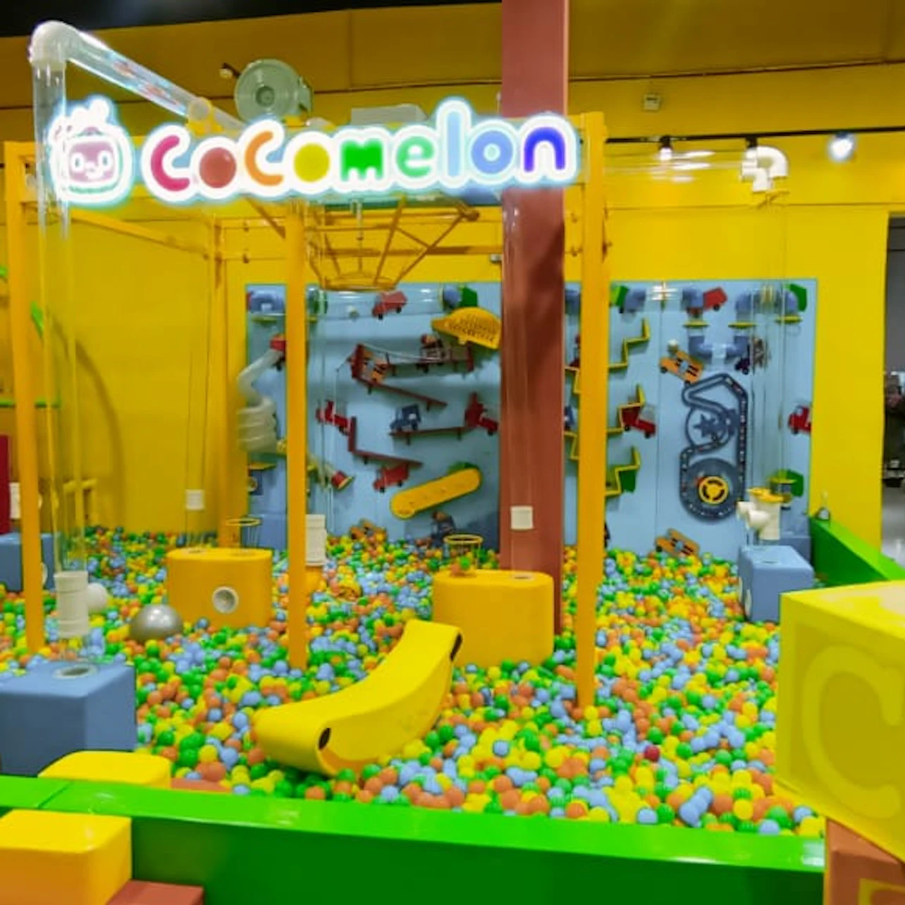 Indoor play area themed with colorful decorations, ball pit, interactive structures, and a "Cocomelon" sign overhead.