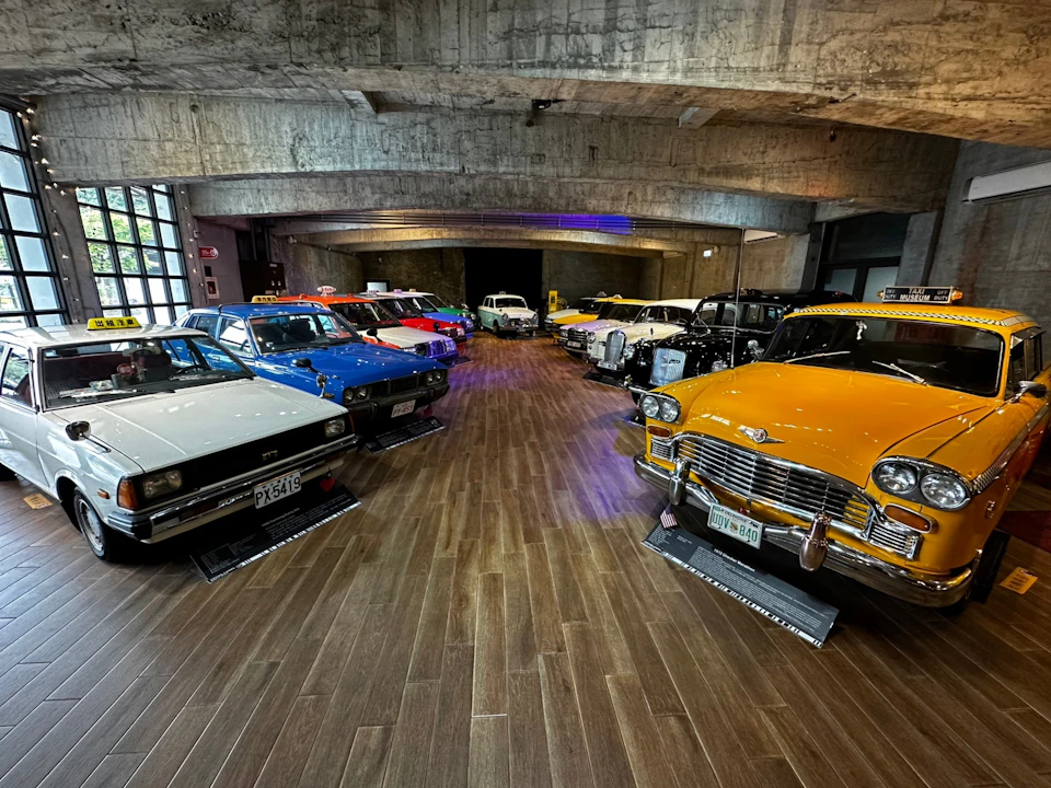 A collection of vintage cars displayed in a showroom with polished wooden floors and a concrete ceiling.