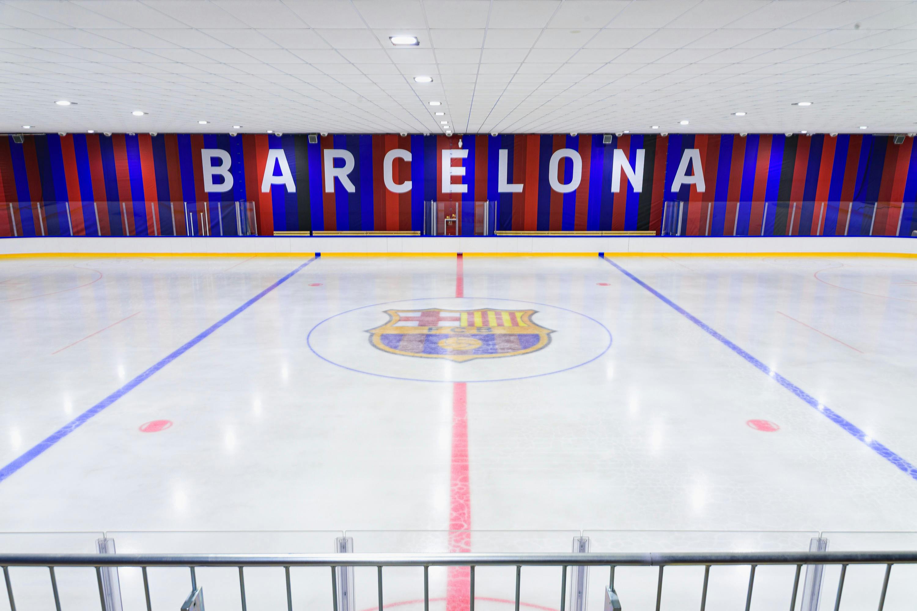 En inomhus ishall med en stor logotyp i mitten is och "Barcelona" visas på en röd och blå randig vägg i bakgrunden.