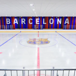 En inomhus ishall med en stor logotyp i mitten is och "Barcelona" visas på en röd och blå randig vägg i bakgrunden.