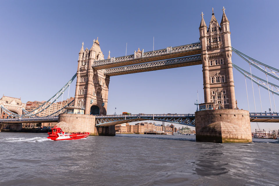 Tower Bridge over the River Thames on a clear day, with a red speedboat in the foreground.
