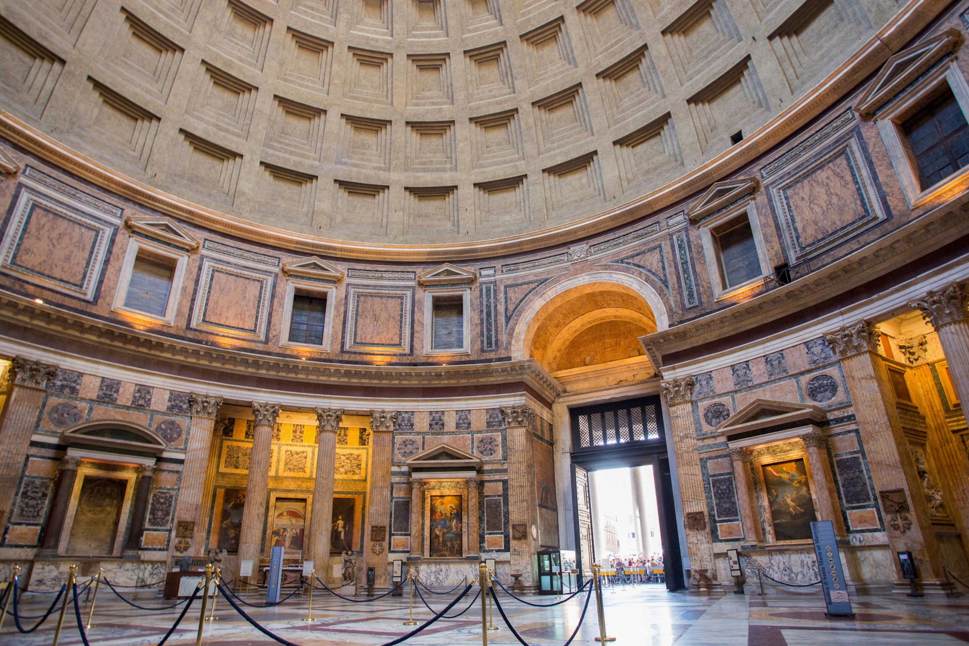 Interior of a large dome with ornate stone walls and a central open doorway allowing natural light in.