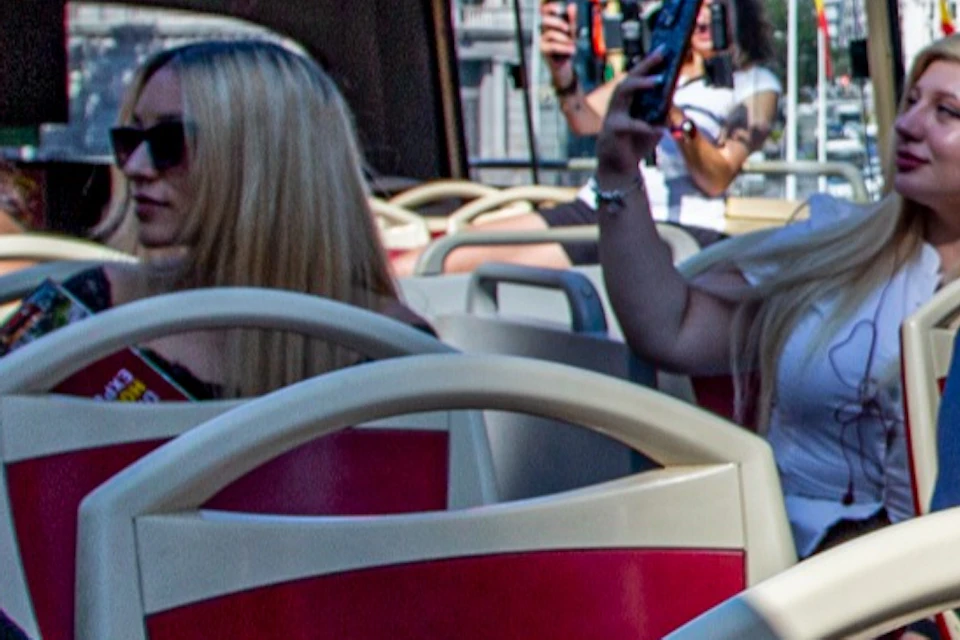 A group of people seated on a double-decker tourist bus under a clear blue sky, with one individual smiling in the foreground.