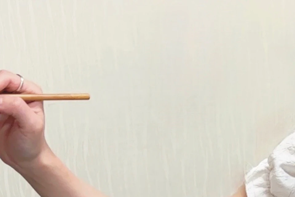A woman applies makeup to a man's lips using a brush. A table with various makeup items is in front of them.