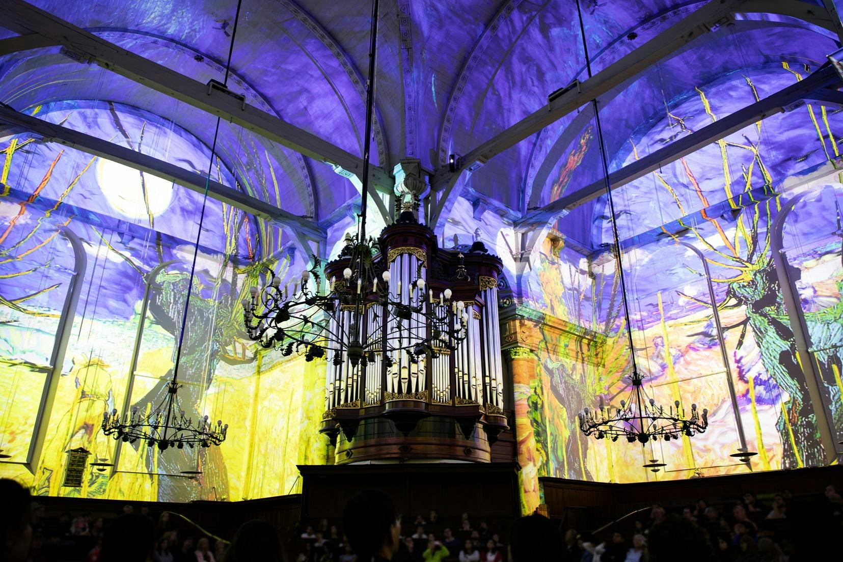 アーチ型の天井と壁に鮮やかでカラフルな投影が施された大聖堂の壮大なオルガン。下には人で溢れています。