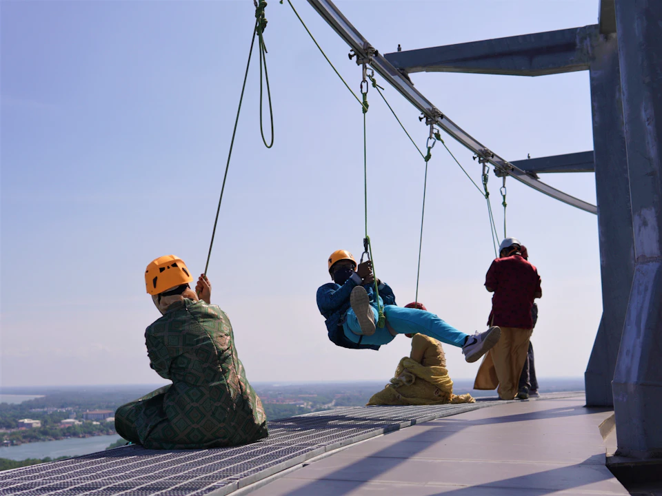 People in safety gear zip-lining from a high structure with a scenic view in the background.