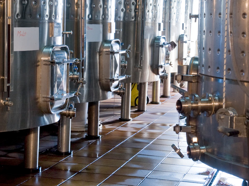 Large stainless steel tanks with glass hatches and valves on a tiled floor, likely in a brewery or industrial facility.