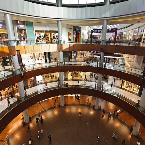 Ein geräumiges, mehrstöckiges Einkaufszentrum mit zahlreichen Geschäften und Menschen, die auf den glasüberdachten Gehwegen spazieren gehen.