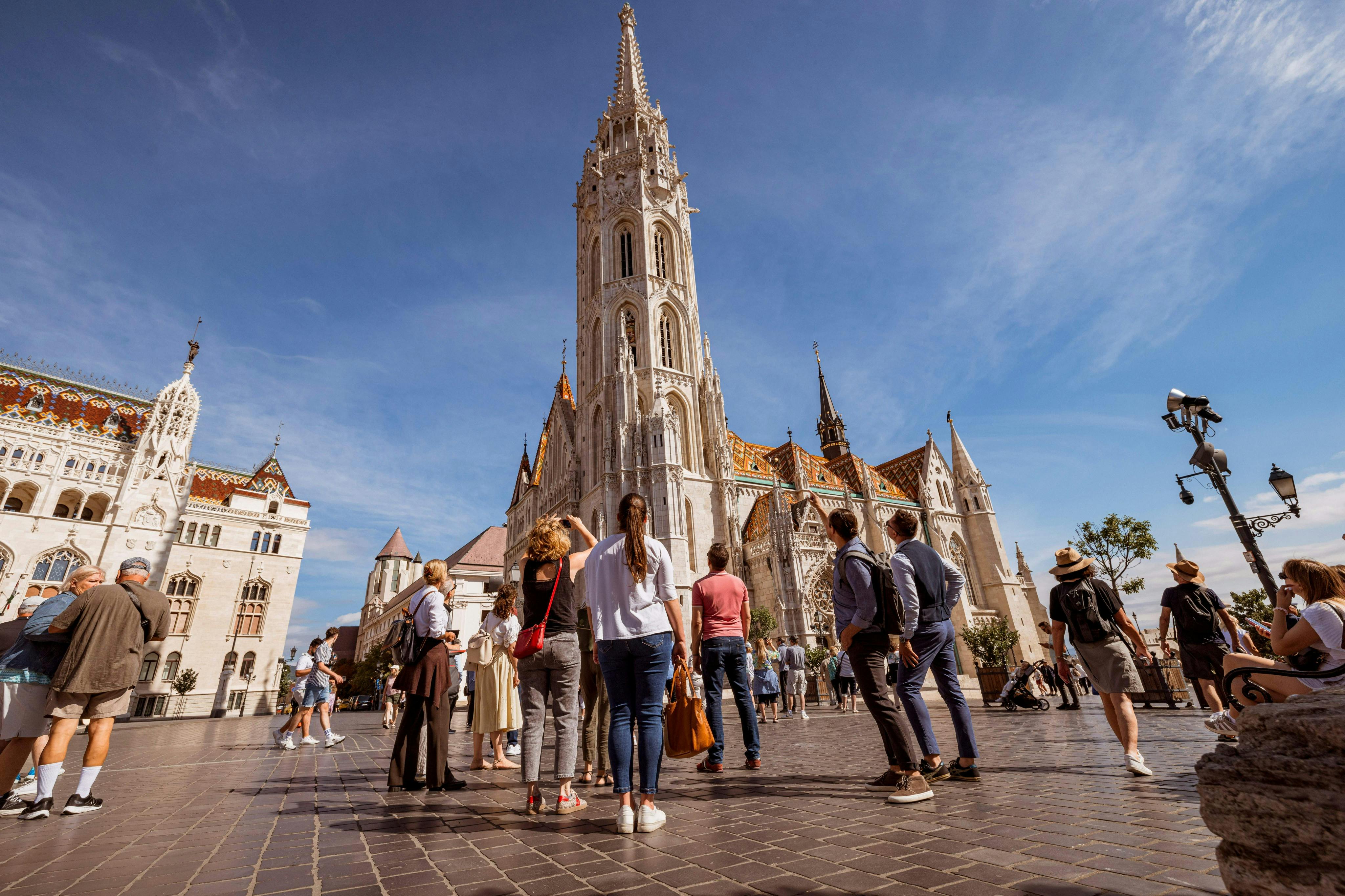 A group of people standing in front of a large Gothic-style church with a tall spire under a clear blue sky.