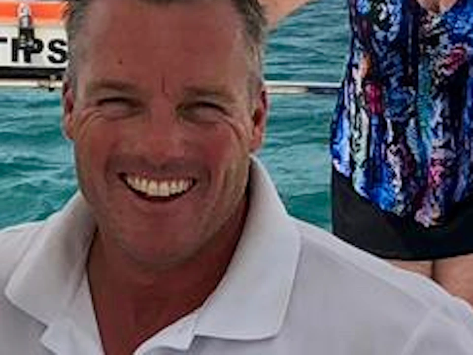 Three people in matching attire stand aboard a boat, smiling at the camera with the ocean in the background.