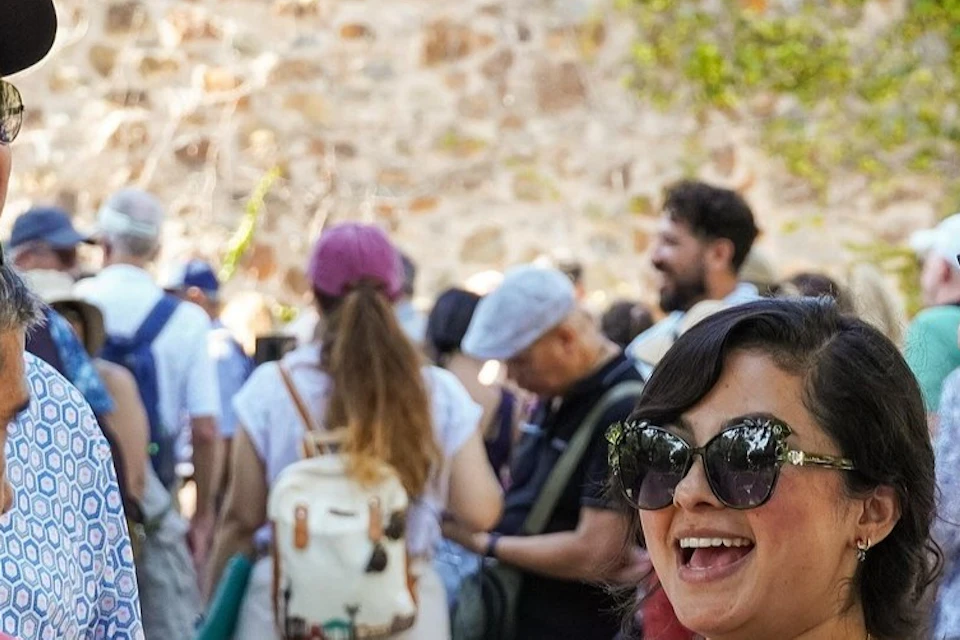 A group of people smiling and talking outdoors, with one person holding a device and wearing a lanyard.