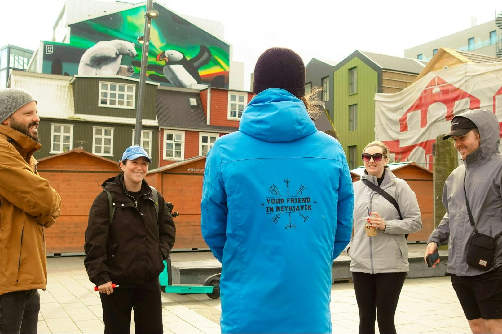 뒤쪽에 글씨가 있는 파란색 재킷을 입은 사람이 다채로운 도시 분위기에서 야외에서 두 사람을 마주보고 서 있습니다.