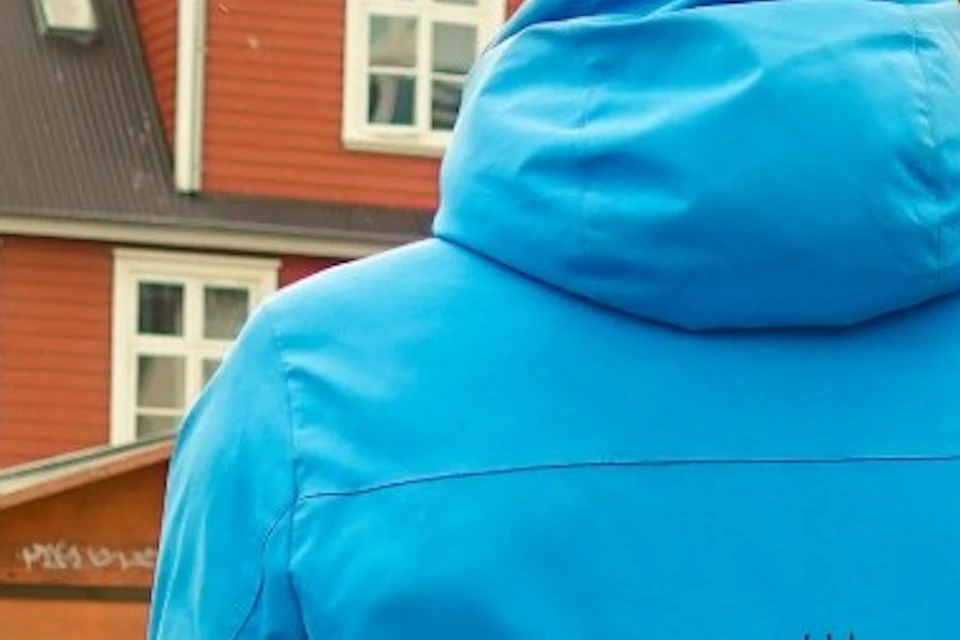 A person in a blue jacket with text on the back stands facing two individuals outdoors in a colorful urban setting.