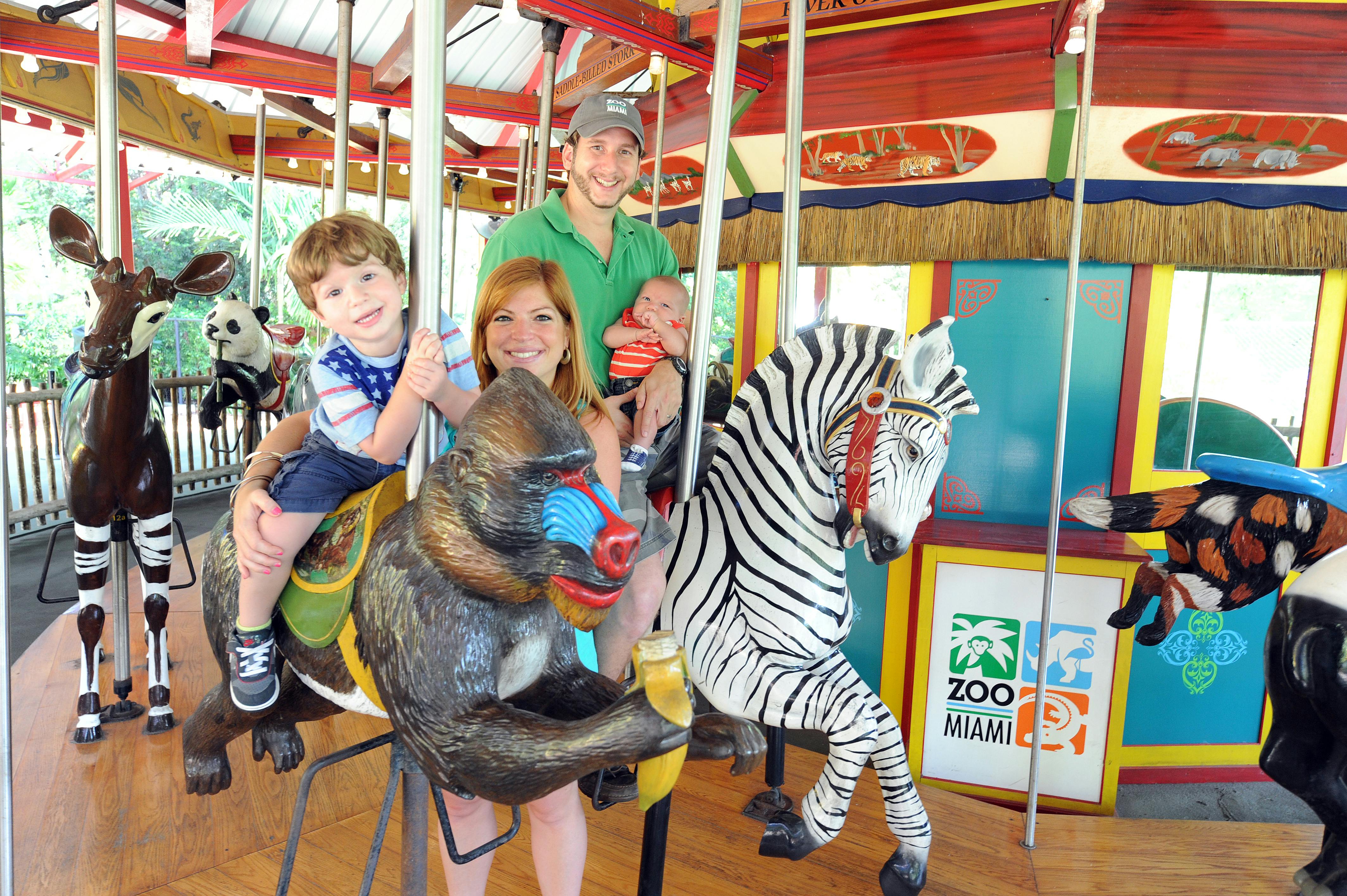 A family of four on a carousel with animal figures including a zebra, gorilla, panda, and antelope.
