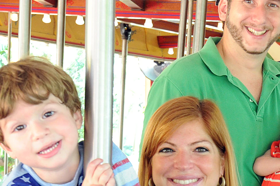 A family of four on a carousel with animal figures including a zebra, gorilla, panda, and antelope.