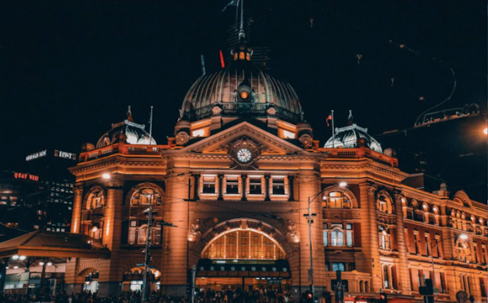 Historic building with a large dome, arched entrance, clock, and illuminated windows at night, featuring intricate architecture.