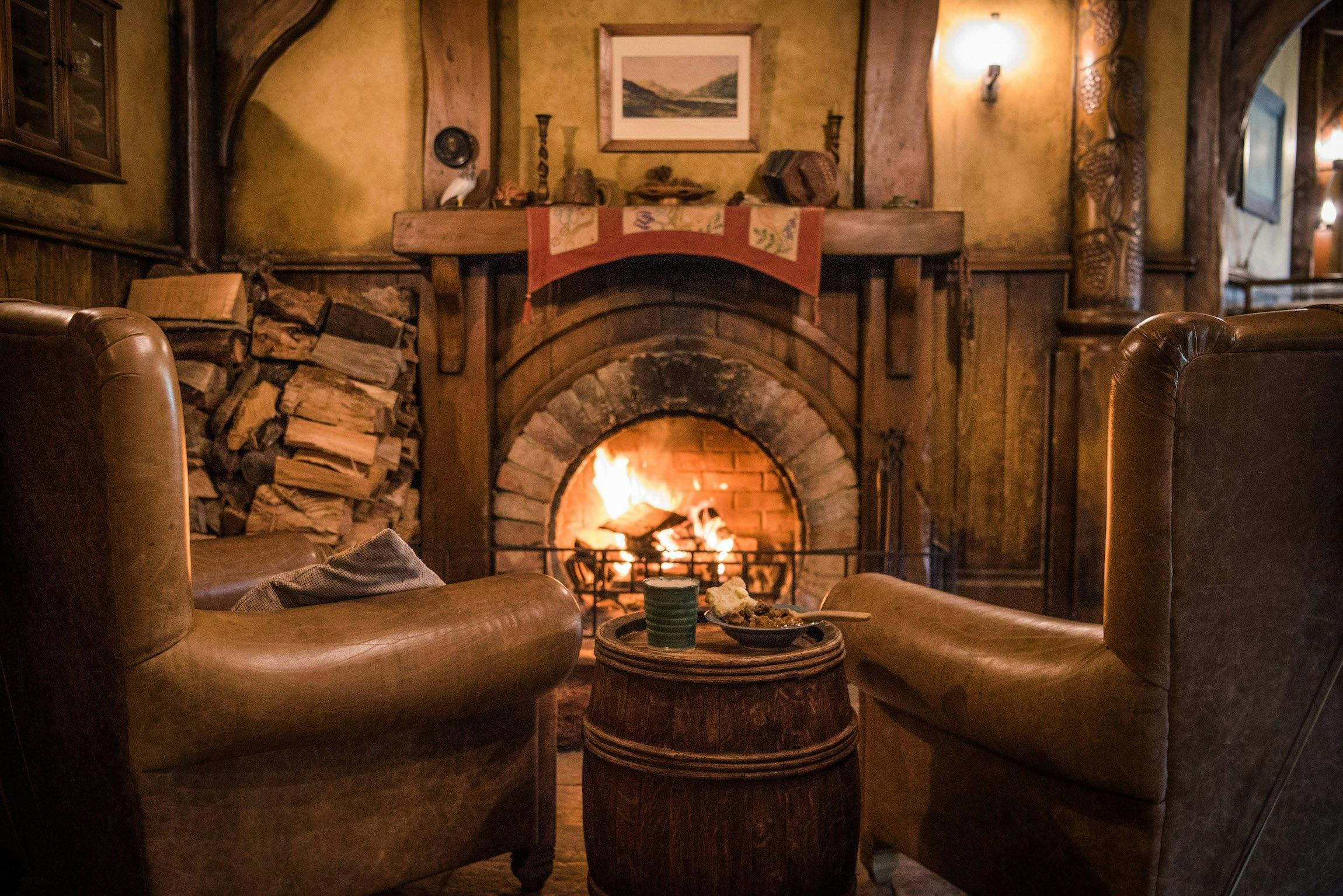 Cozy living room with a lit fireplace, two armchairs, a wooden table with a candle, and rustic decor.