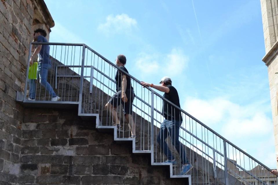 Two people ascending outdoor stone stairs with a metal railing under a blue sky.