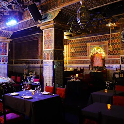 En svagt upplyst, utsmyckad restaurang med mönstrade kolumner, röda tygstolar, dukade matbord och invecklade väggdesigner.