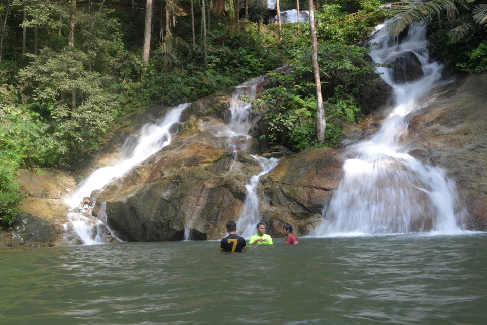 Three people standing in water near a rocky waterfall surrounded by lush greenery.