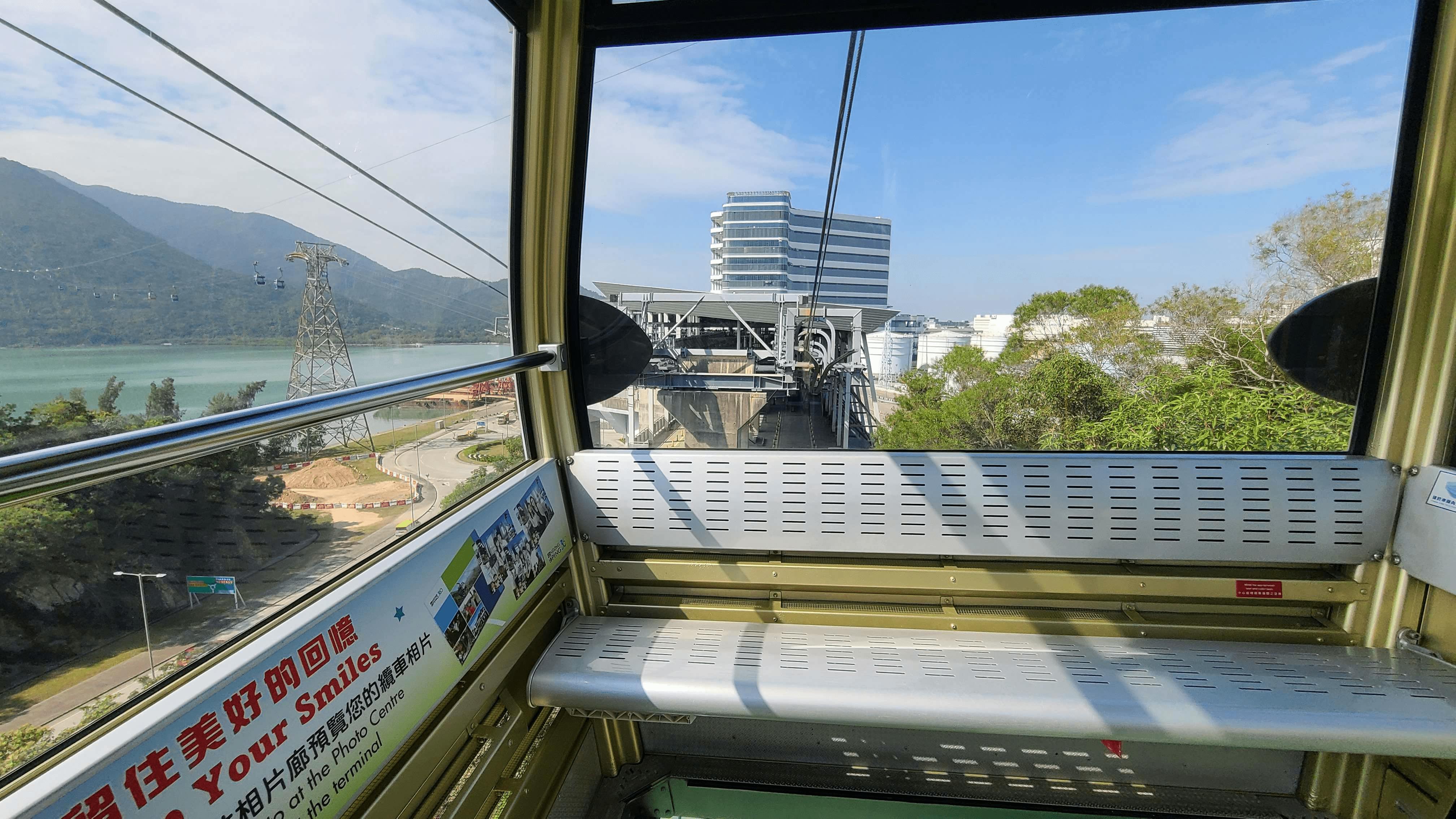 View from inside a cable car approaching a station, showing buildings, trees, and distant mountains under a blue sky.