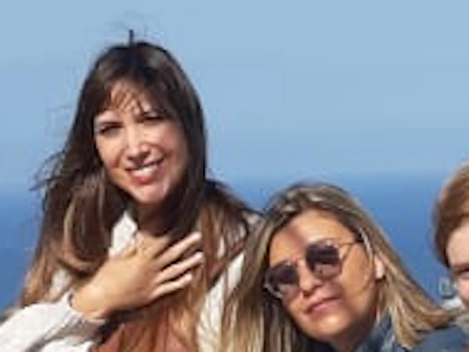 Five people smile and pose on a stone structure with a coastal city and ocean in the background on a clear day.