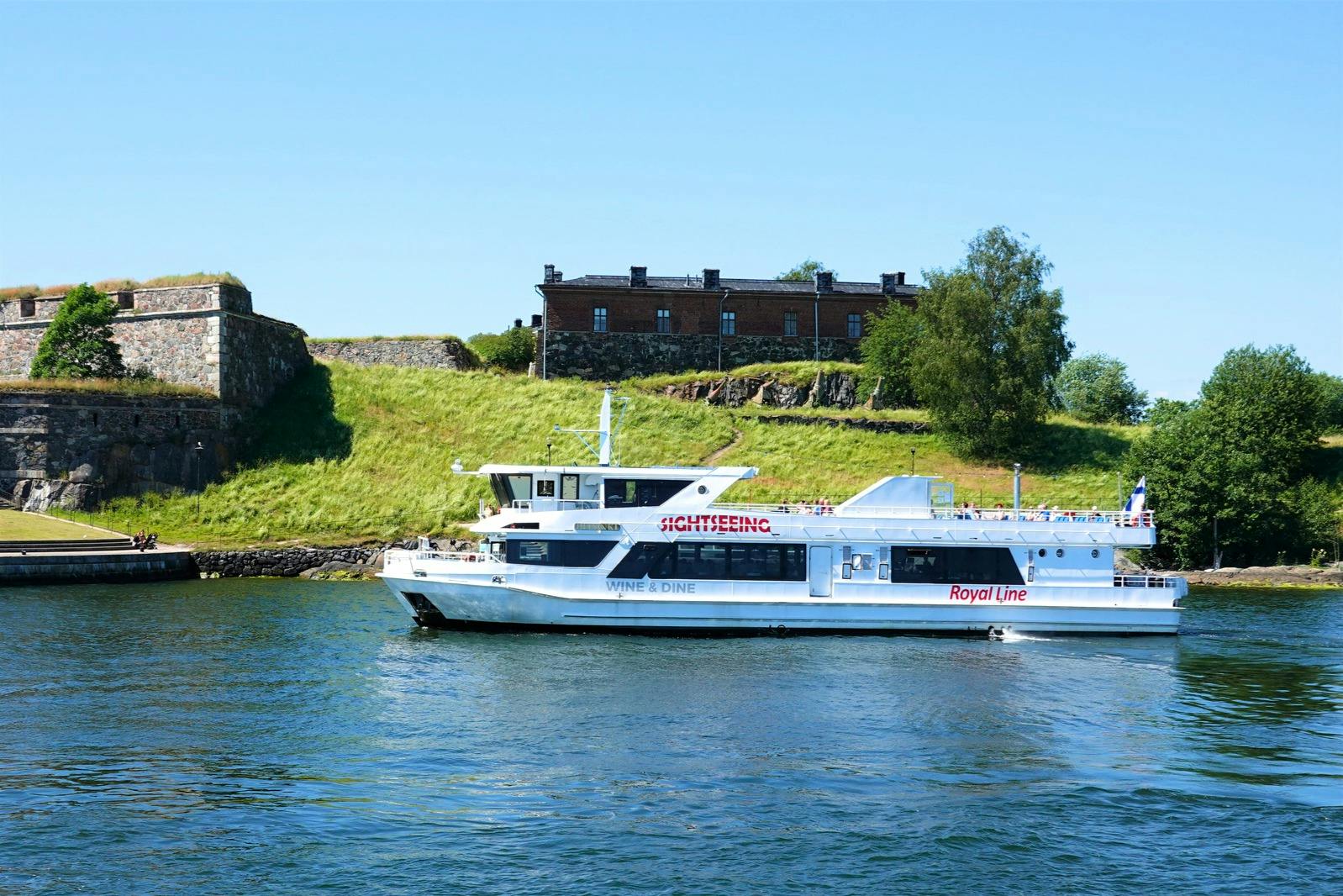 A white sightseeing boat labeled "Royal Line" passes by a green hillside with a historic brick building on a clear day.