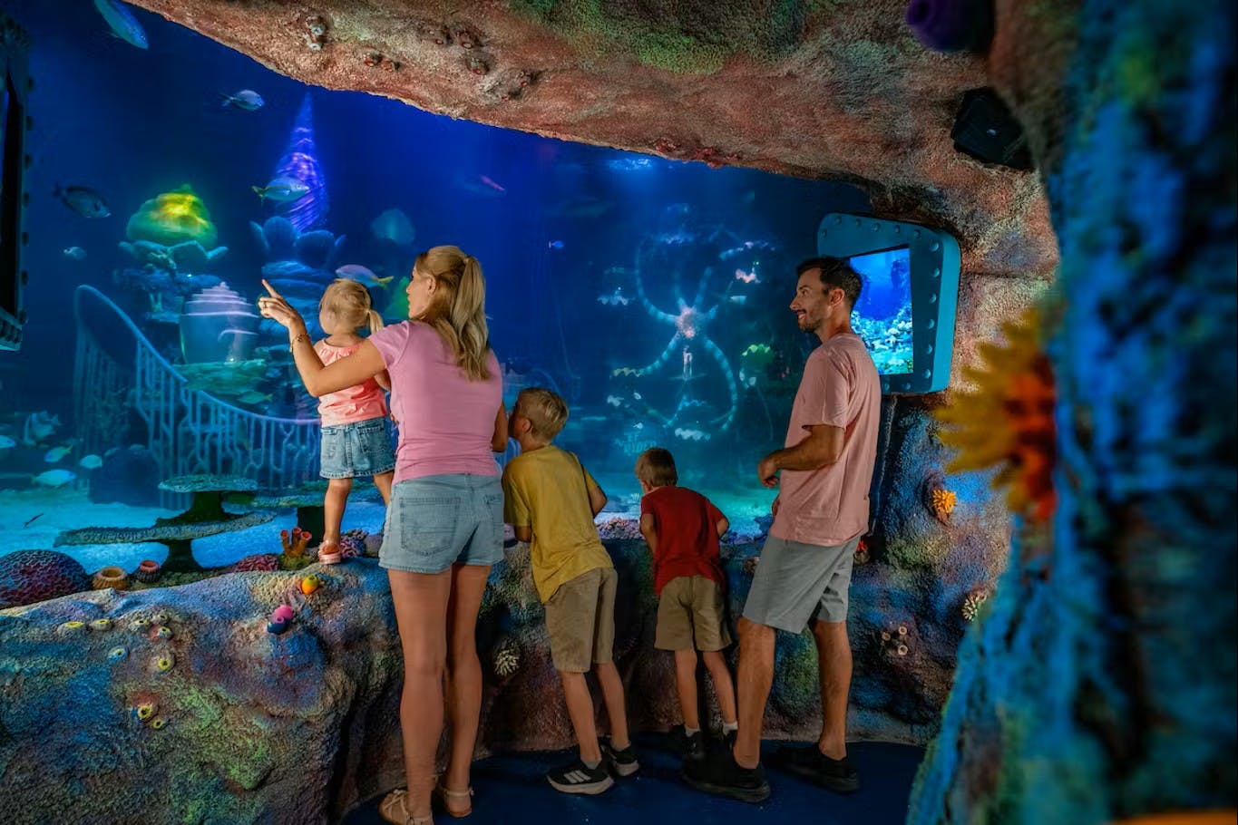 A family observes marine life through a large aquarium display in a room decorated like an underwater cave.