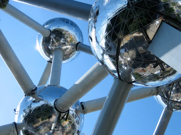 Zbliżenie na strukturę Atomium, ukazujące jego odblaskowe stalowe kule połączone cylindrycznymi rurkami na czystym błękitnym niebie.