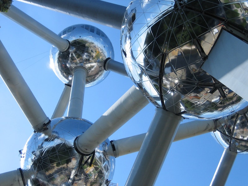 Zbliżenie na strukturę Atomium, ukazujące jego odblaskowe stalowe kule połączone cylindrycznymi rurkami na czystym błękitnym niebie.