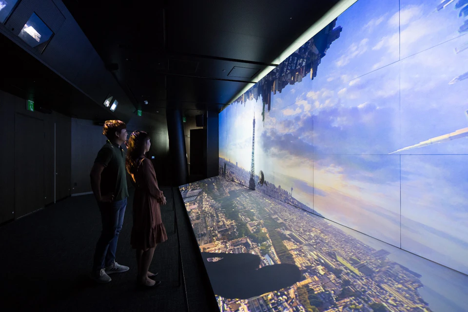 Two people observe a large digital screen displaying an inverted cityscape, featuring the Eiffel Tower prominently.