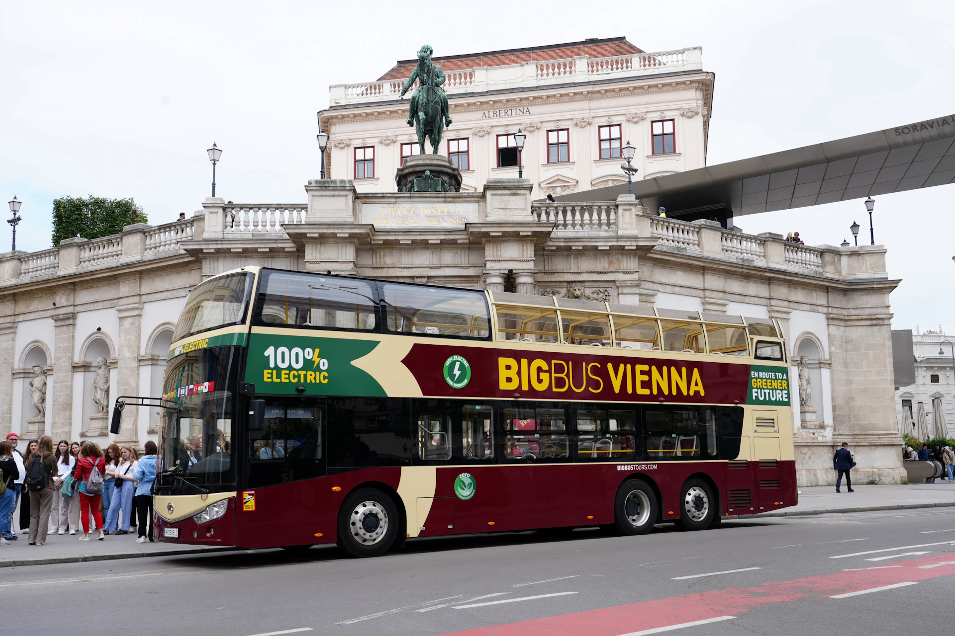 A red and cream electric double-decker tour bus labeled "Big Bus Vienna" parked near a historical building.