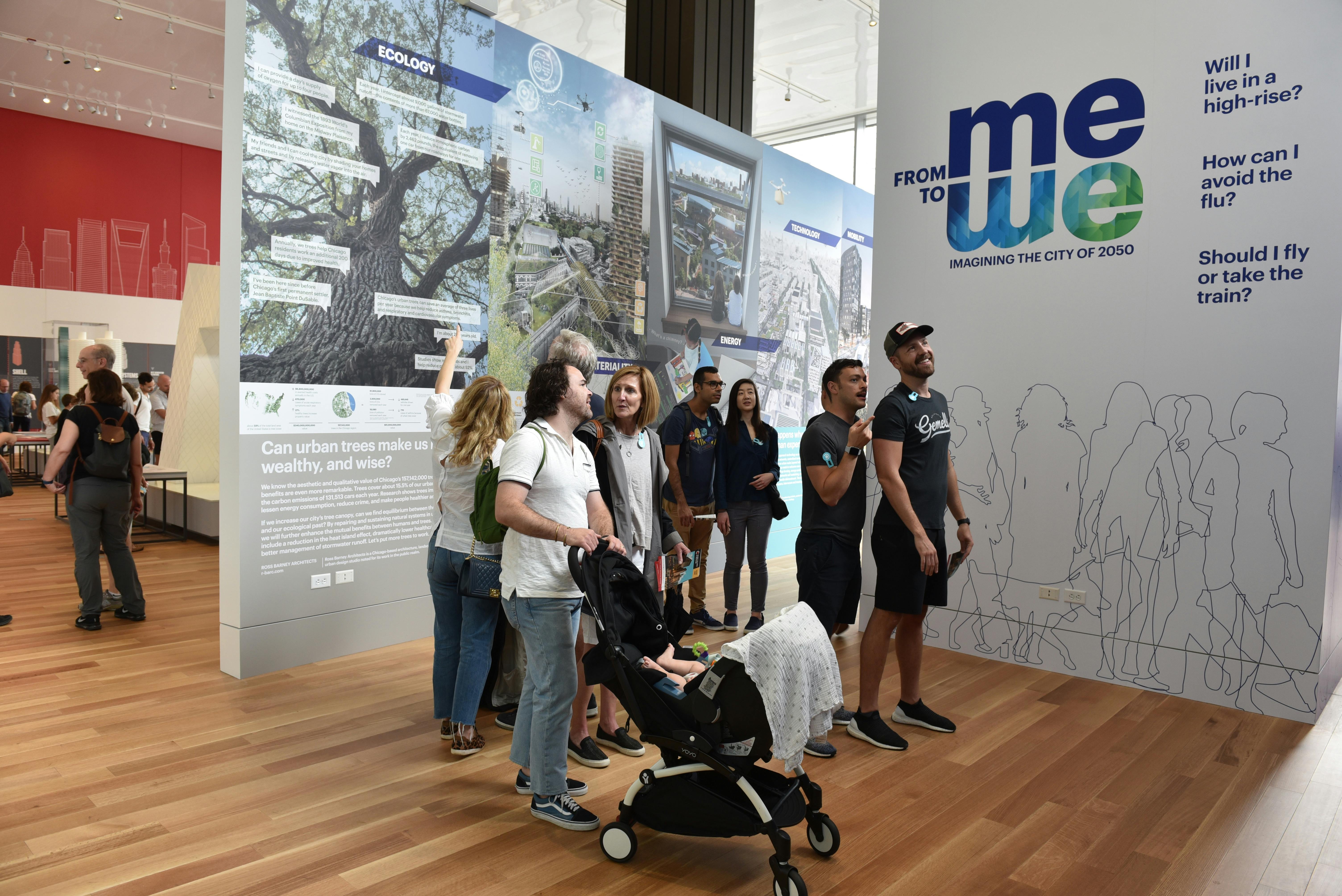 People exploring an exhibit about urban ecology and city planning, with informative graphics on the walls and a stroller in the foreground.