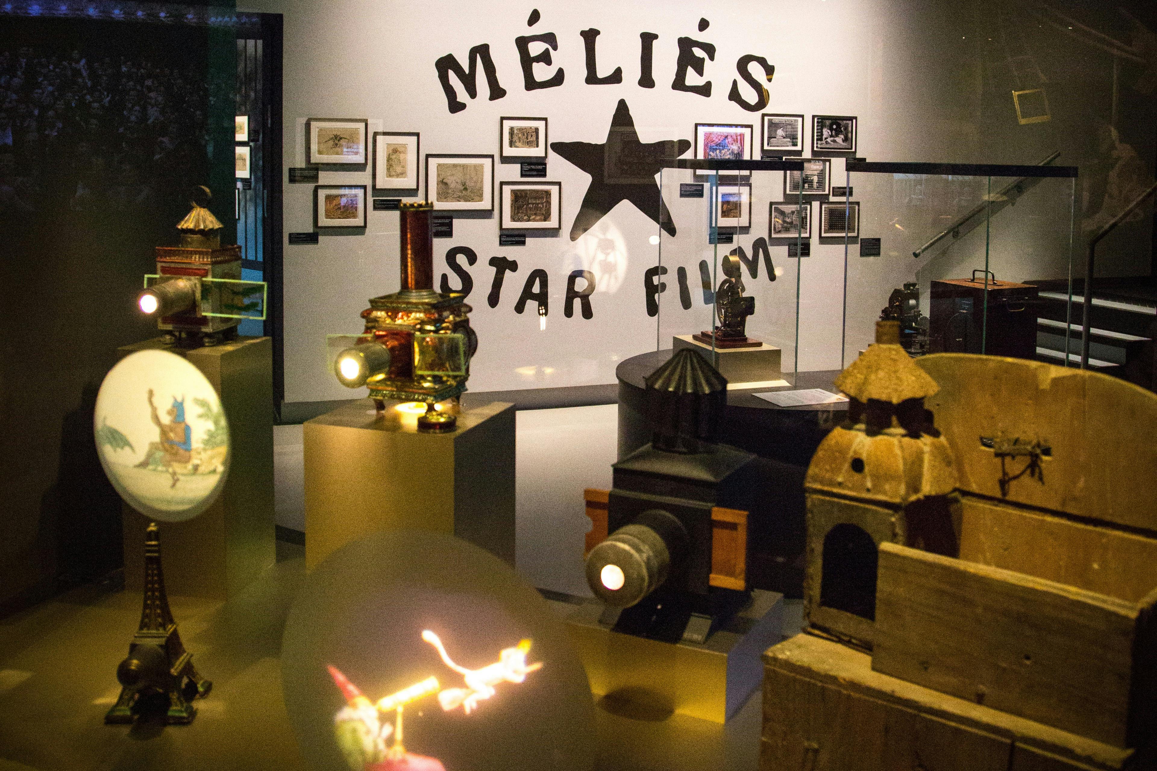 Έκθεμα με πρώιμο κινηματογραφικό εξοπλισμό και αναμνηστικά, με το λογότυπο "Méliès Star Film" και κορνιζαρισμένες εικόνες στον τοίχο.