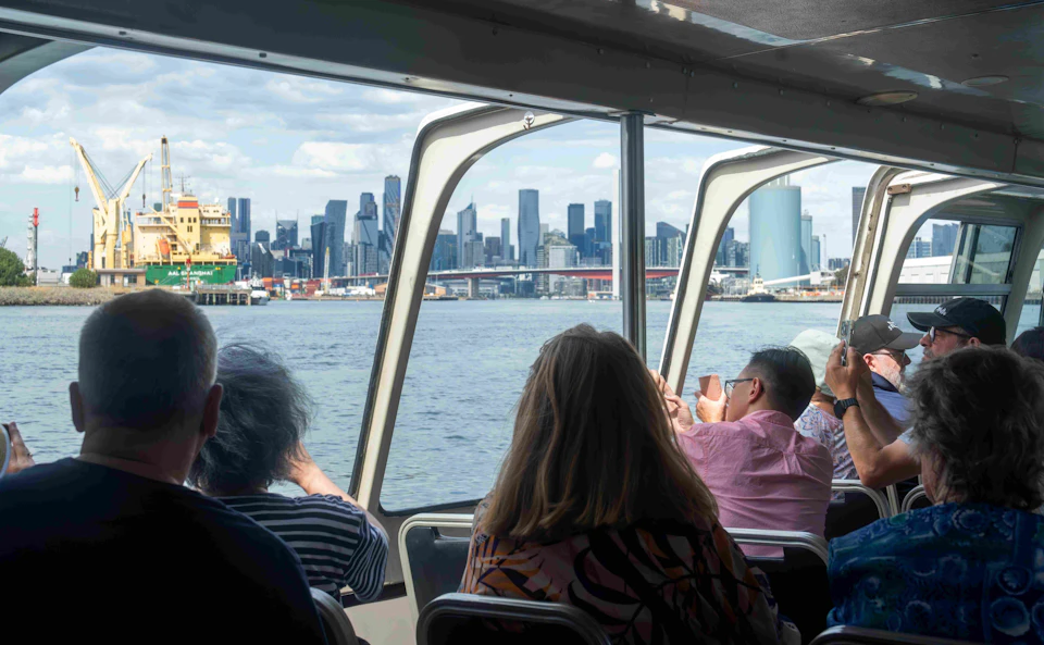 Passengers on a boat looking at a city skyline through large windows on a clear day.