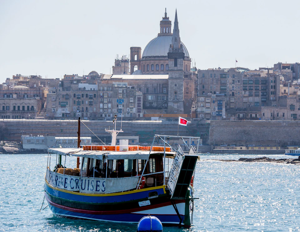 A boat labeled "Harbour & Sea Cruises" floats on the water with a historic city and a large dome in the background.