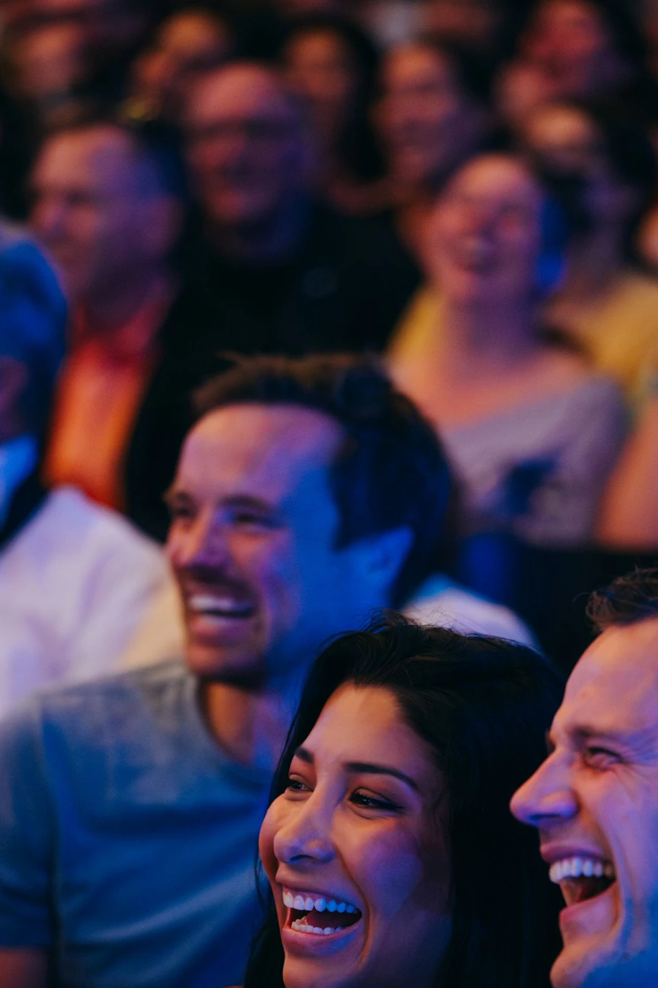 A group of people sitting closely together, smiling and laughing in a lively atmosphere with colorful lighting.
