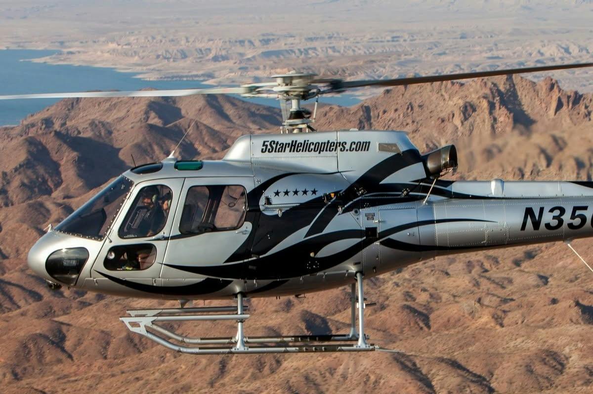 A silver helicopter with black patterns and the text "5StarHelicopters.com" flying over a desert landscape.