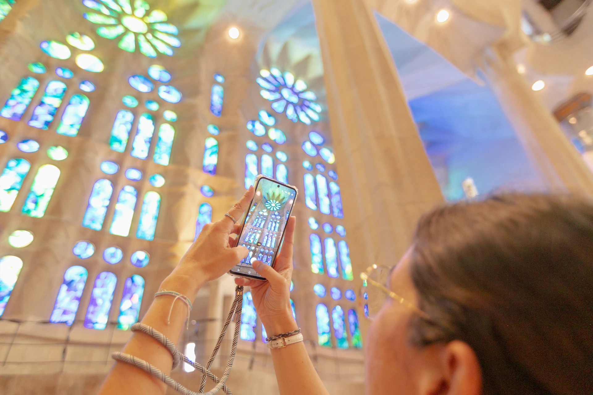 A person holding a phone capturing colorful stained-glass windows inside a cathedral.