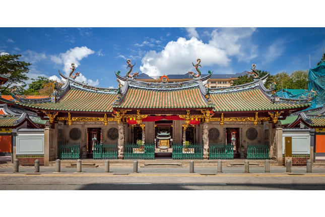 Ornate temple with decorative roof, intricate carvings, and red lanterns, under a blue sky with scattered clouds.
