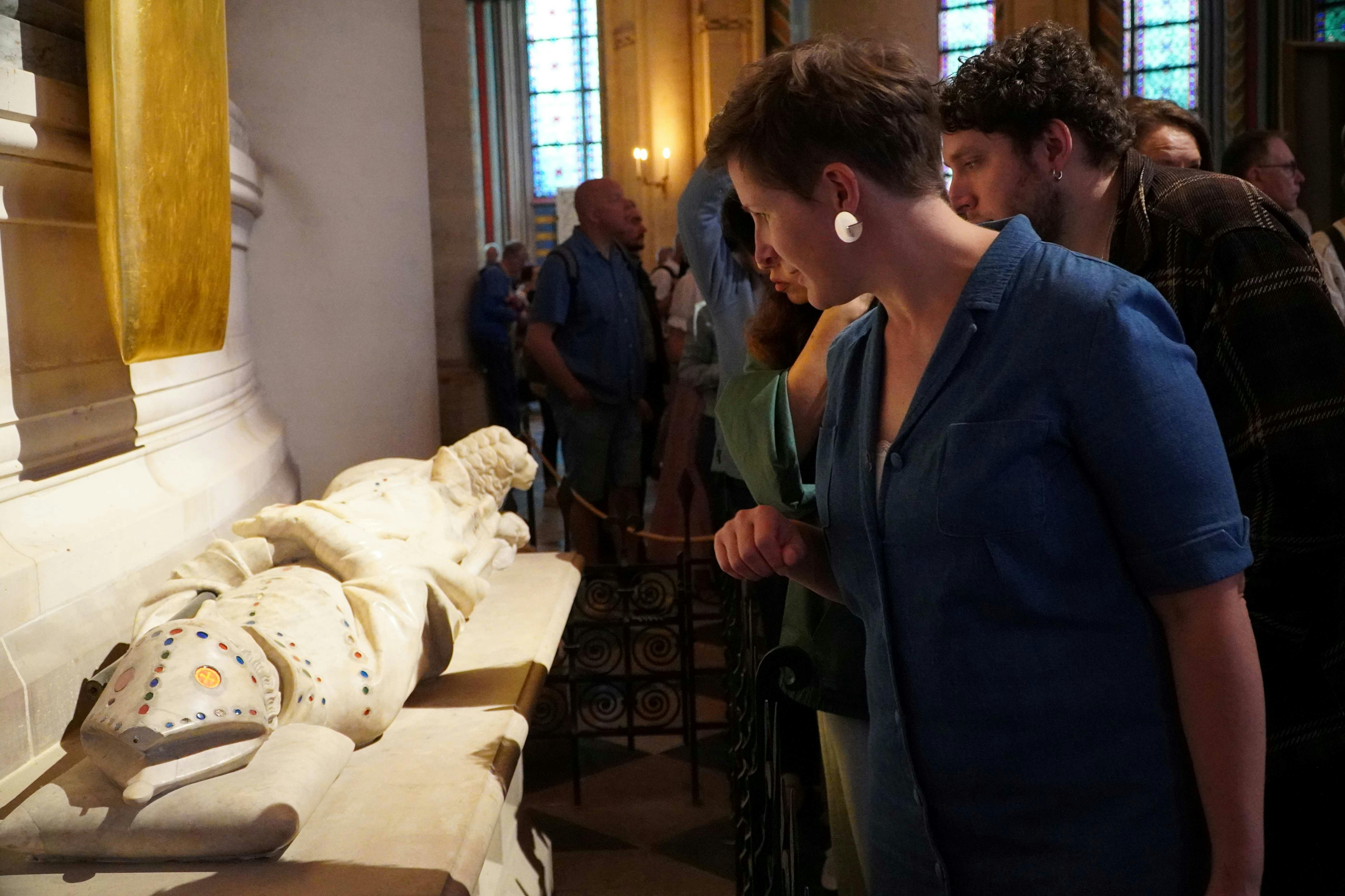 人们在博物馆里观看白色大理石雕塑，背景是彩色玻璃窗。