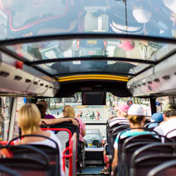 Passagerarna sitter på ett övre däck på en buss med ett glastak, med utsikt över en stadsgata med cyklister utanför.