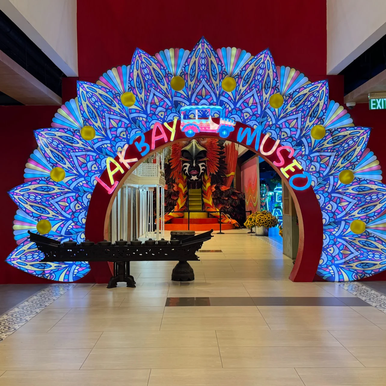A colorful archway with the text 'Lakbay Museo' leads into an exhibit featuring vibrant decorations and a large mask display.