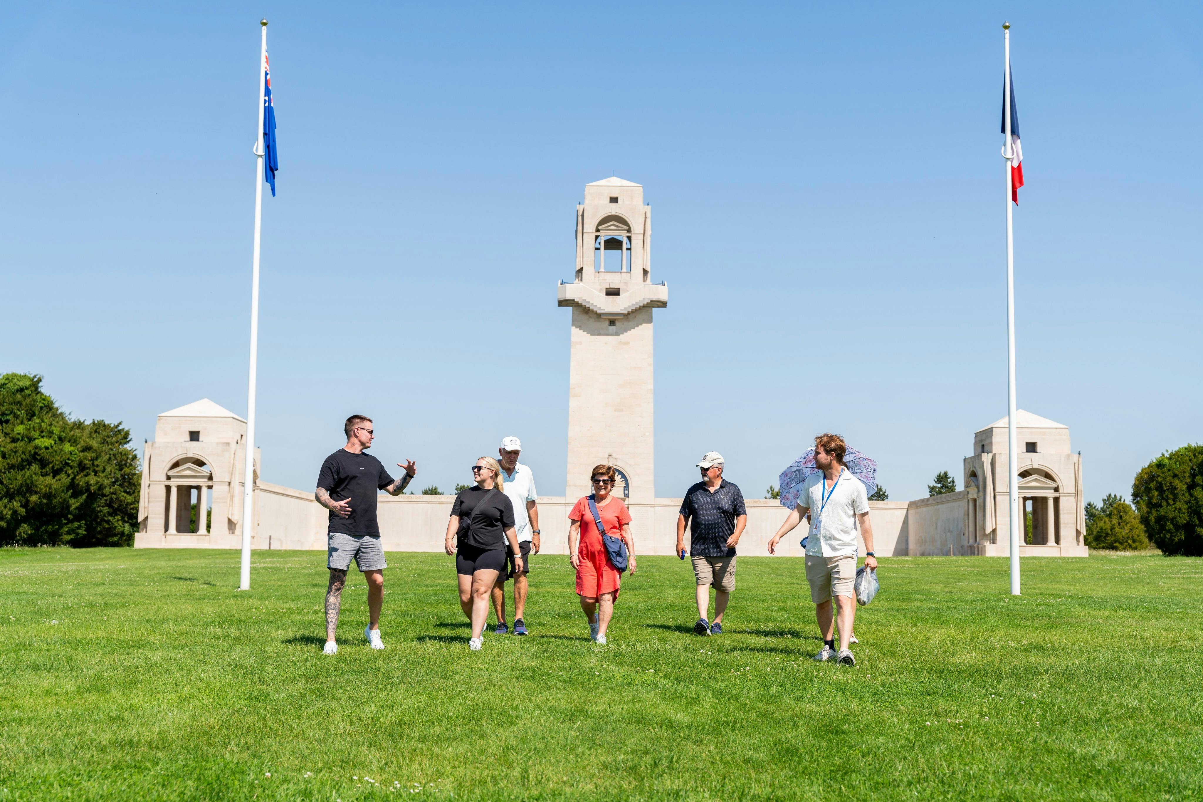A group of people walking on grass near a tall stone monument and flagpole on a clear, sunny day.