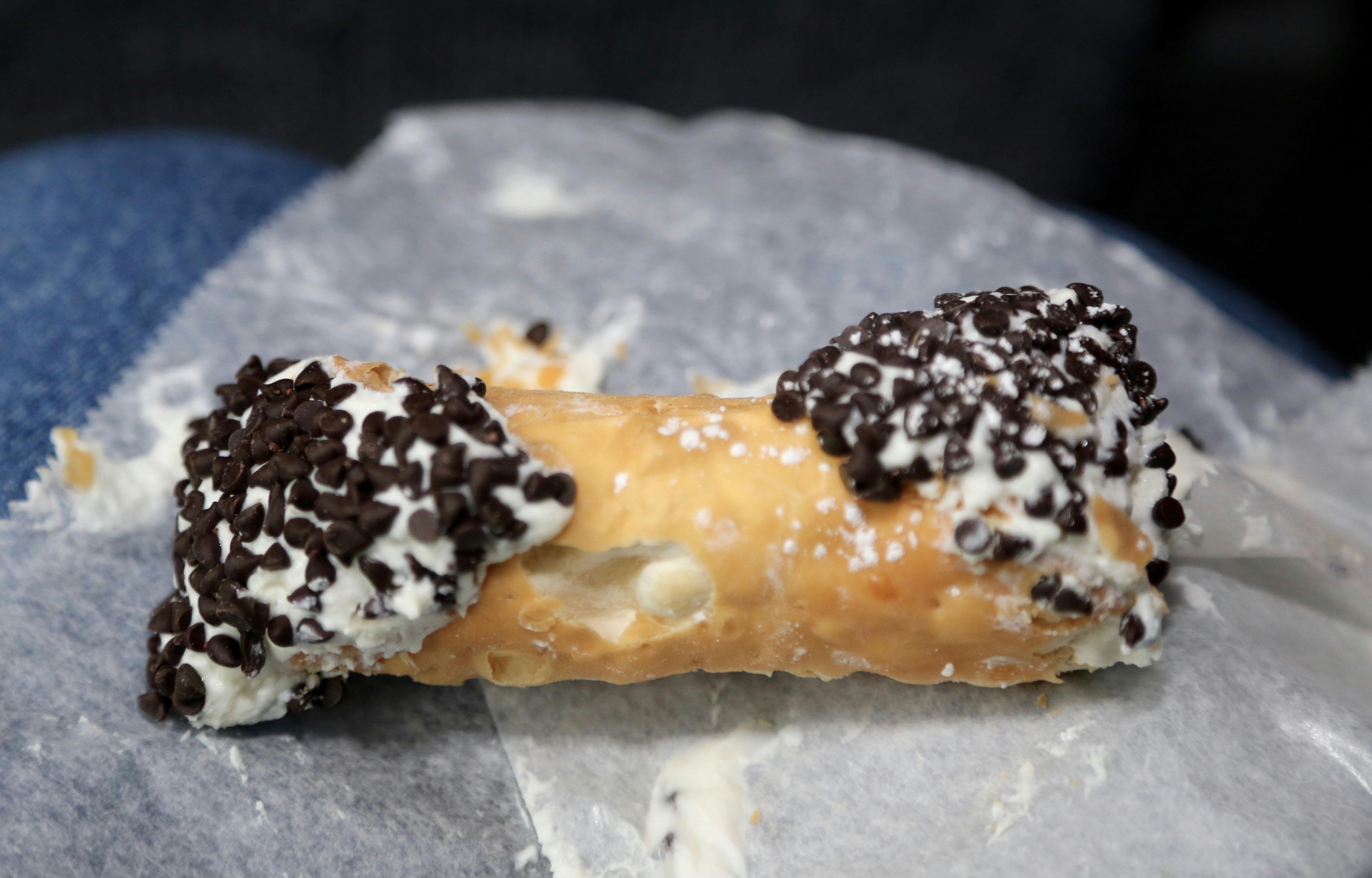 A cannoli filled with creamy filling, topped with chocolate chips on either end, rests on a piece of parchment paper.