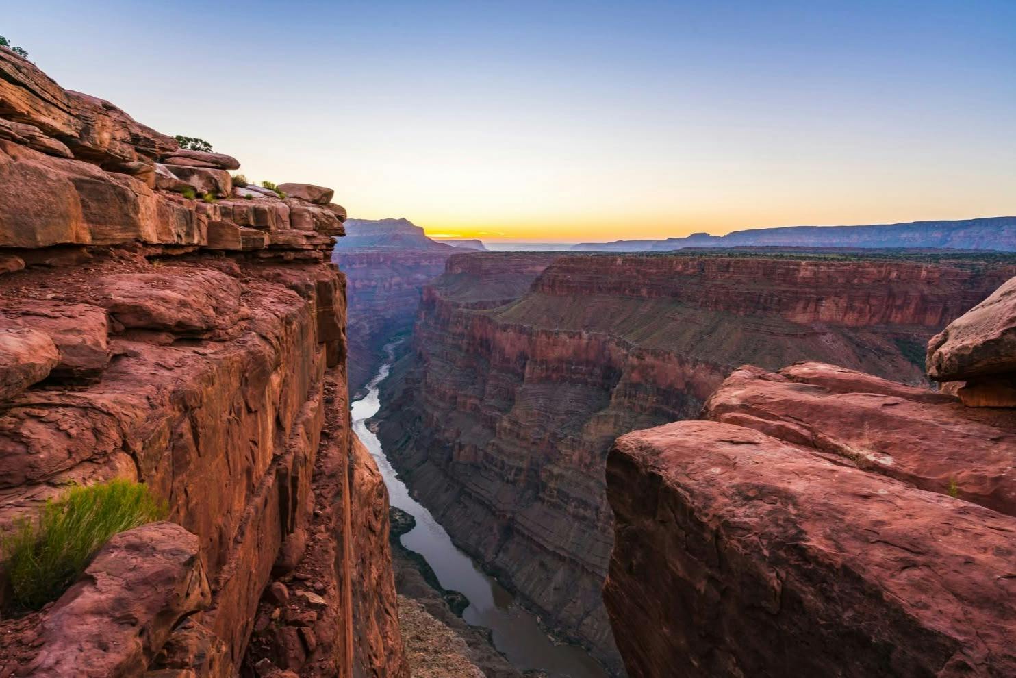 A view of a canyon at sunset with rocky cliffs and a river running through the valley below.