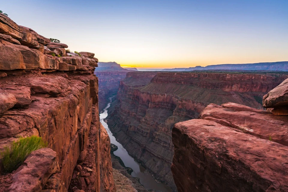 A view of a canyon at sunset with rocky cliffs and a river running through the valley below.